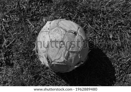 Black and white photo of old soccer ball. Classic soccer ball on the grass. Broken and used football