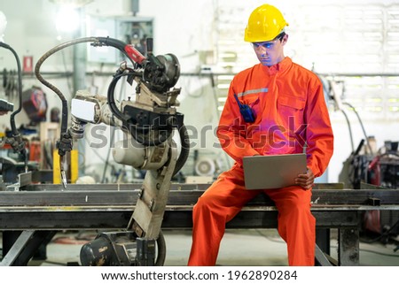 Male engineer use laptop computer setting welding robot in factory.