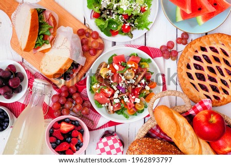 Summer picnic food table scene with cold salads, sandwiches, fruit and treats. Overhead view on a white wood background. Copy space.