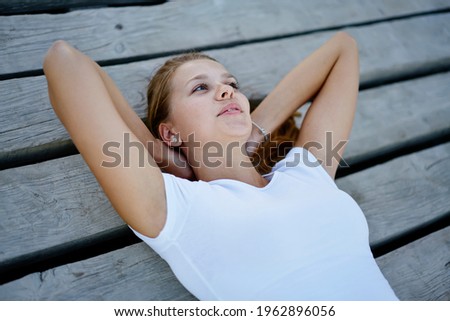 Carefree hipster girl enjoying time at wooden pier thinking about fashion modeling outdoors, attractive female teenager dressed in t-shirt with copy space for brand name or label feeling thoughtful