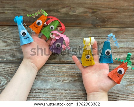 Kids Craft, a fun monster with one eye made out of an egg box and colored paper, is dressed on children's fingers.