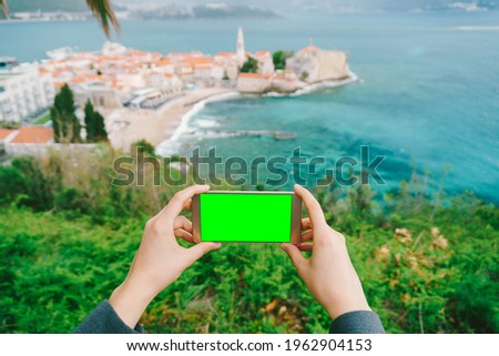 Hands are holding a smartphone with a blank screen. In the distance is the old town. Montenegro