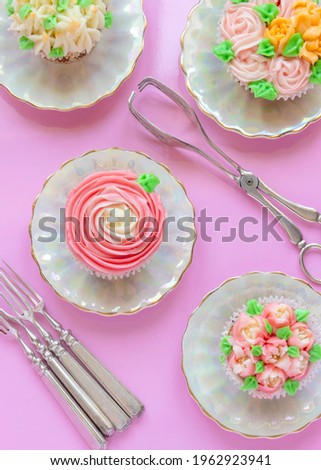 vertical overrview image of pretty delicately cup cakes iced with  Russian  piping icing tips ,pink background  and silverware with copy space
