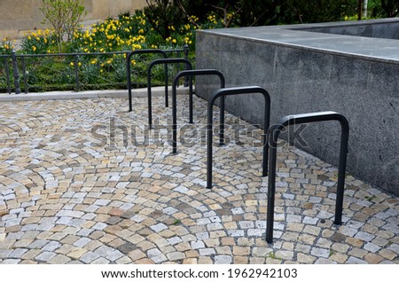 bicycle stand in the shape of a rectangle with round corners urban environment of solid black metal on the ground paving of granite cubes modern furniture to store and lock the motorcycle or scooter 
