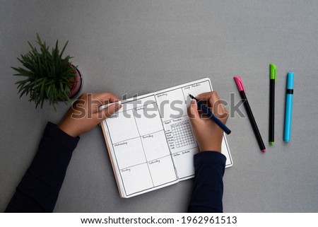 Journaling daily for mental well being and personal development. Weekly planner set up on a minimal grey table top, with sketch pens and a plant Royalty-Free Stock Photo #1962961513