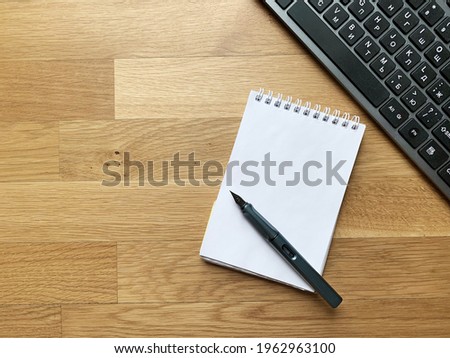 part of keyboard with blank notepad and pen on wooden surface top view. selective focus on notepad.