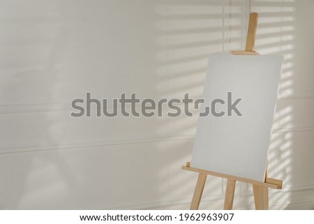 Wooden easel with blank canvas on light background. Space for text
