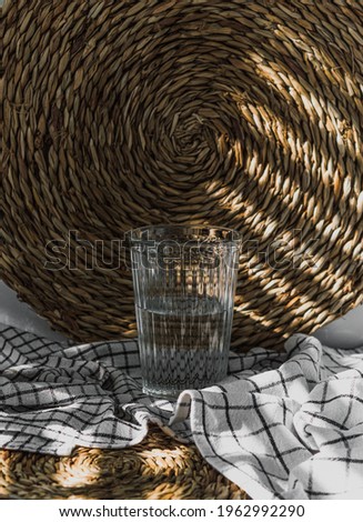 Still life of a glass of water with texture, above a white linen kitchen cloth and a natural fiber braided pad
