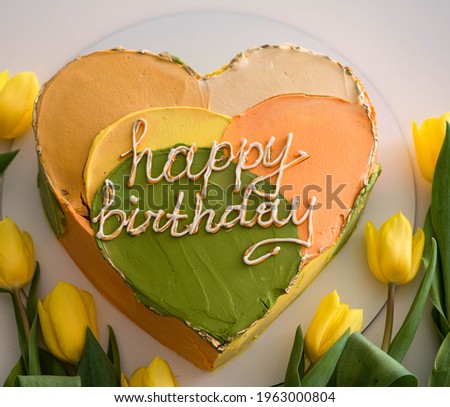Birthday cake in the form of a heart with multi-colored cream and flowers on a wight background