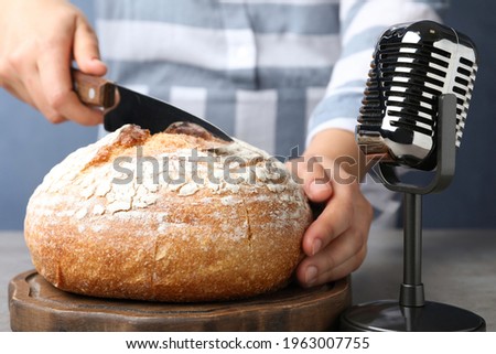 Woman making ASMR sounds with microphone and bread at grey table, closeup