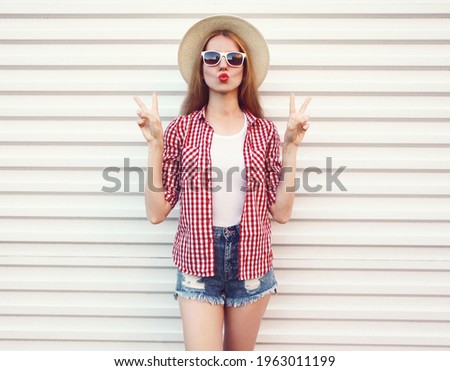 Portrait of beautiful woman blowing her red lips sending sweet air kiss wearing a summer straw hat on a white background