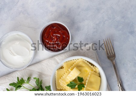 Ravioli with cheese with parsley and ketchup and sour cream on a light background with space for an inscription