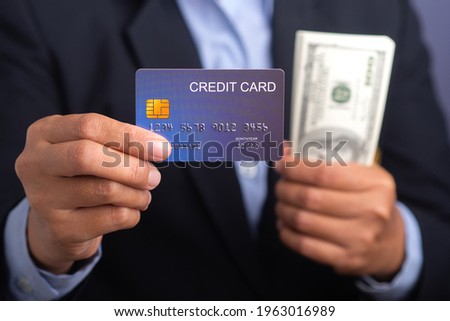Businessman holding a mockup blue credit card and US banknote while standing in a studio with copy space for text. Close-up photo. Money and business concept.