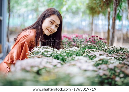 A beautiful woman dressed in a brown dress in the middle of a forest rich in colorful flowers, beautiful during daytime, touring the flower garden and taking pictures for relaxing and happy vacation.