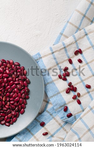 Red beans in a plate on a checkered towel on a white textured background. The view from the top.