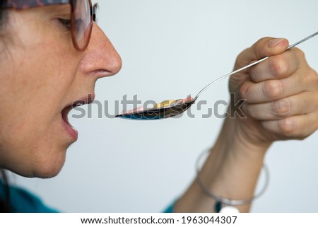 Middle-aged woman takes a spoon full of pills. Concept of drug addiction or need to take many drugs.