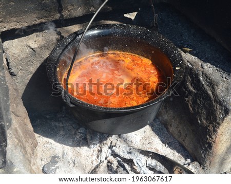Cast iron copper hangs over an open fire. Cooking fish soup.