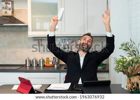 Portrait of joyful young businessman raising both arms for a deal at dawn. Expressive home worker rejoices in the kitchen. Happiness, successful meeting and contract signing.