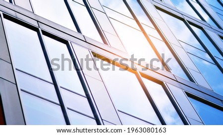 Blue sky reflection in glass facade of building. View of office building windows close up with sunrise, reflection and perspective..Bright sunny day with sunbeams on the blue sky.Velvia graphic filter