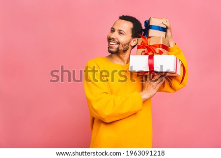 Cheerful smiling african american man holding wrapped present boxes. Happy black young man congratulating, giving birthday gift, isolated on pink background.