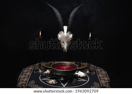 Pentagram and devil symbols with black burning candles on witch wooden table in the dark. Esoteric, gothic and occult background, Halloween mystic concept.