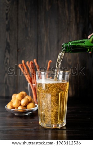Jet of beer out of the bottle is poured into a beer glass, causing a lot of bubbles and foam, black wooden background