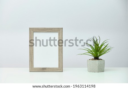 White marble desk with vertical photo frame and a plant in concrete flower pot near a gray wall.