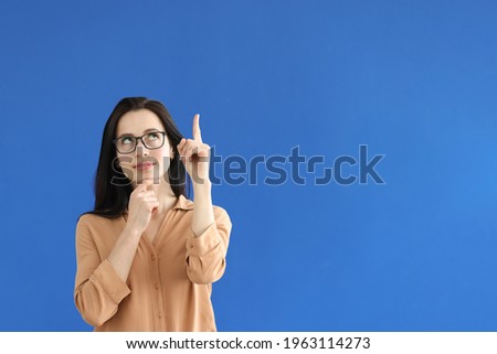 Pensive woman in glasses showing index finger up on blue background