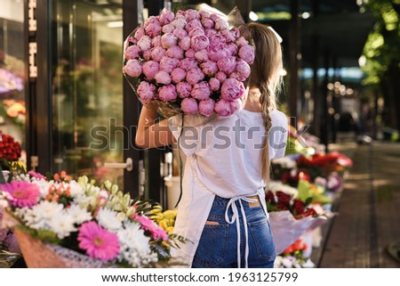 Young  woman florist with a heap of pink peony flowers in her little flower shop Royalty-Free Stock Photo #1963125799
