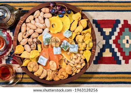 Mix of Turkish sweets, nuts and dried fruits - pears, figs, pineapples on wooden platter. Glasses with sweet tea on the table. Flat view of oriental sweets, plate with dessert, mock up with copy space
