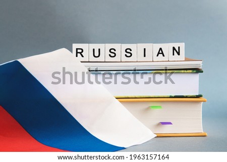the inscription russian on a stack of textbooks, books, exercise books and national flag of Russia, the concept of education and learning foreign languages. Royalty-Free Stock Photo #1963157164