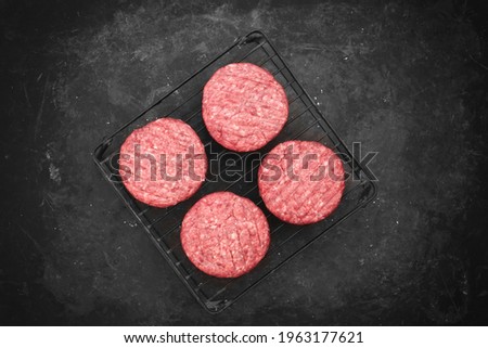 Barbecue Grate with Raw Beef Hamburger Patties. Ground Beef Patties for Grilling and Roasting. Raw Minced Steak Burgers from Beef Meat on Black Background. Burger Cutlets On Paper And Grate.
