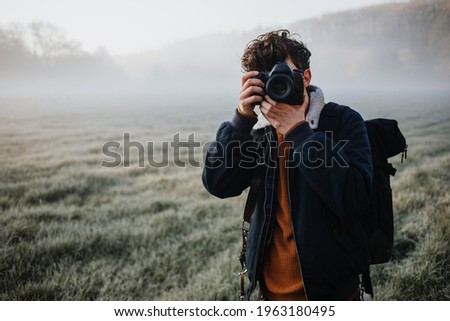 Young Photographer on a foggy meadow camera is covering the face 