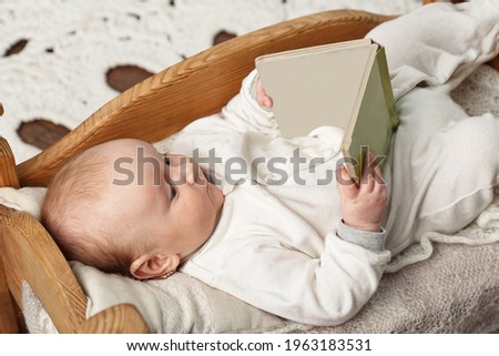 A cute adorable baby carefully reads and looking a book on the toy small bed. Development and education. Early learning concept. Mock up for text or picture.