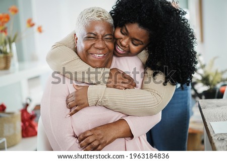 African daughter hugging her mum indoors at home - Main focus on senior woman face Royalty-Free Stock Photo #1963184836