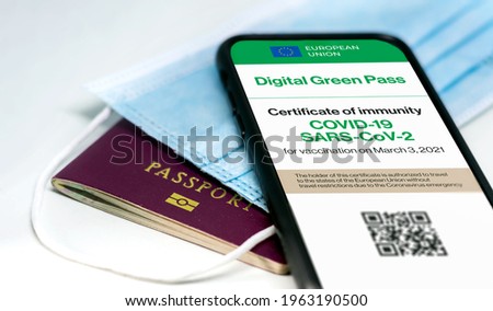 The digital green pass of the european union with the QR code on the screen of a mobile phone over a surgical mask and a passport. Immunity from Covid-19. Travel without restrictions. Royalty-Free Stock Photo #1963190500