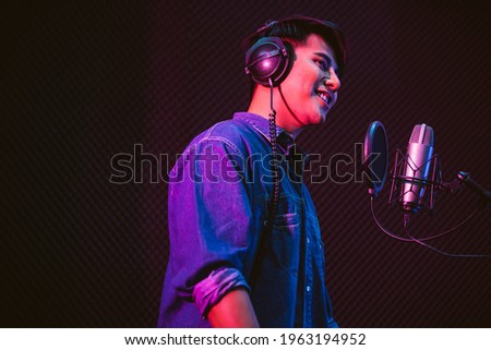 Asian male singer recording songs by using a studio microphone and pop shield on mic with passion in a music recording studio. Performance and show in the music business. Image with copy space.
