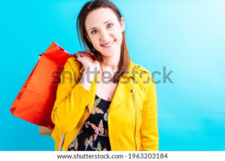 Beautiful young woman in yellow jacket on blue background holding colorful shopping bags. she shopaholic concept. Shopping weekend. sale