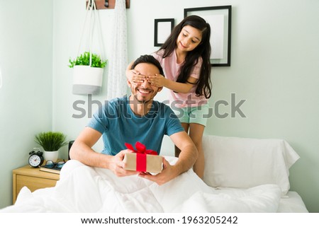 Close your eyes for a surprise. Beautiful girl giving a present to her dad for his birthday. Little daughter and young dad celebrating Father's Day 