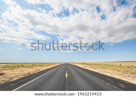 A straight road of blacktop going to a vanishing point in the open and flat country of Grant County in Eastern Washington State.  The cloud layer above is broken with pockets of blue sky
 Royalty-Free Stock Photo #1963219453