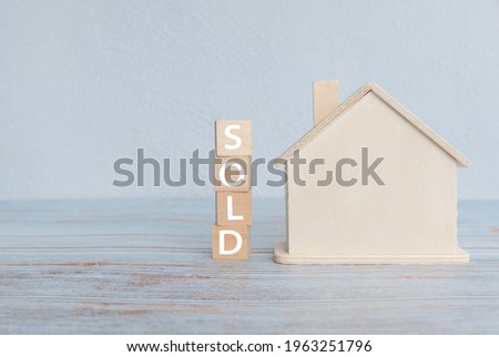 Concept of selling property or real estate with model of wooden house and a stack of word SOLD.