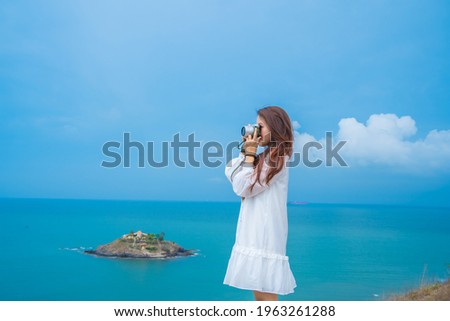 Focus happy young woman wearing white dress holding a camera to taking pictures for keeping memories of trip.  travel concept.