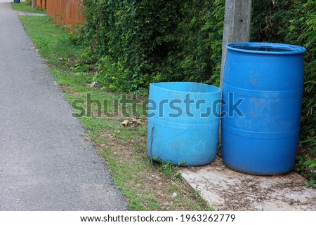 Two large blue plastic trash cans are located on an outdoor pavement area for littering.