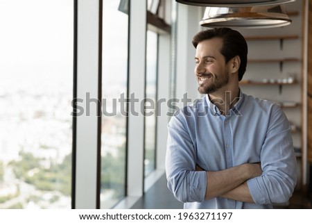 Happy young Caucasian businessman look in window distance planning or thinking of perspectives and opportunities. Smiling male employee dream or visualize career success. Business vision concept. Royalty-Free Stock Photo #1963271197