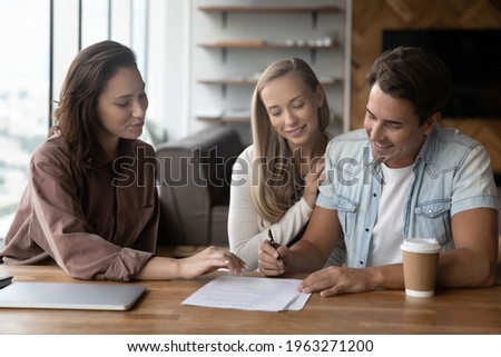 Excited young Caucasian man and woman sign paper contract close deal with realtor or broker at meeting in office. Happy couple buyers clients put signature on document make agreement with agent.