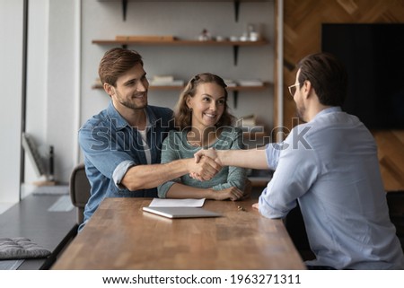 Smiling young couple buyers shake and get acquainted greet with relator or broker at office meeting. Happy man and woman clients handshake close deal or make agreement with real estate agent. Royalty-Free Stock Photo #1963271311