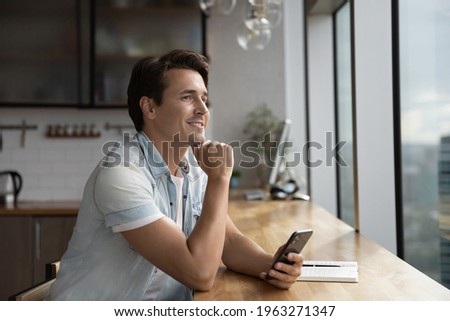 Pensive Caucasian man use cellphone look in distance thinking or making plans. Thoughtful dreamy male browse text on smartphone visualize or imagine opportunities perspectives. Vision concept.