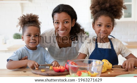 Two happy kids and mom cooking in kitchen together, cutting fresh vegetables, preparing organic salad for healthy dinner. Mom teaching children to male vegetarian meal. Head shot family portrait