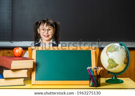 Little elementary school girl in classroom interior. Books, globe, apple, pencils, marker board, chalk board. Lots of space for text, messages, advertising.