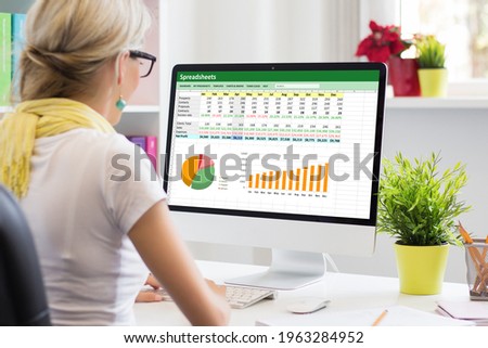 Woman working with data and graphs in spreadsheet document on desktop computer Royalty-Free Stock Photo #1963284952